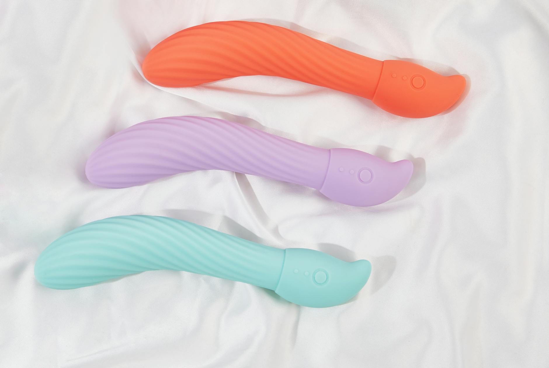 Three colorful clitoral vibrators arranged on white fabric, showing smooth texture and design variety