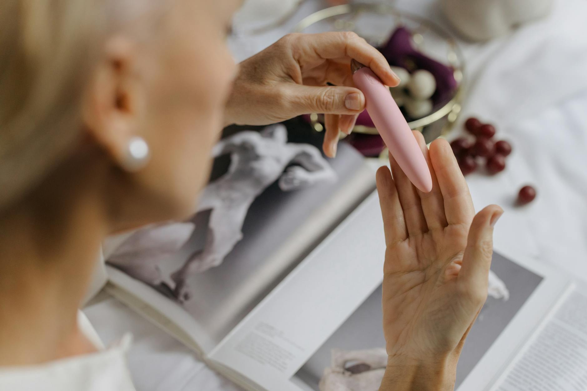 Close-up of a woman holding a pink lemon vibrator with art books in the background, emphasizing intimate self-discovery