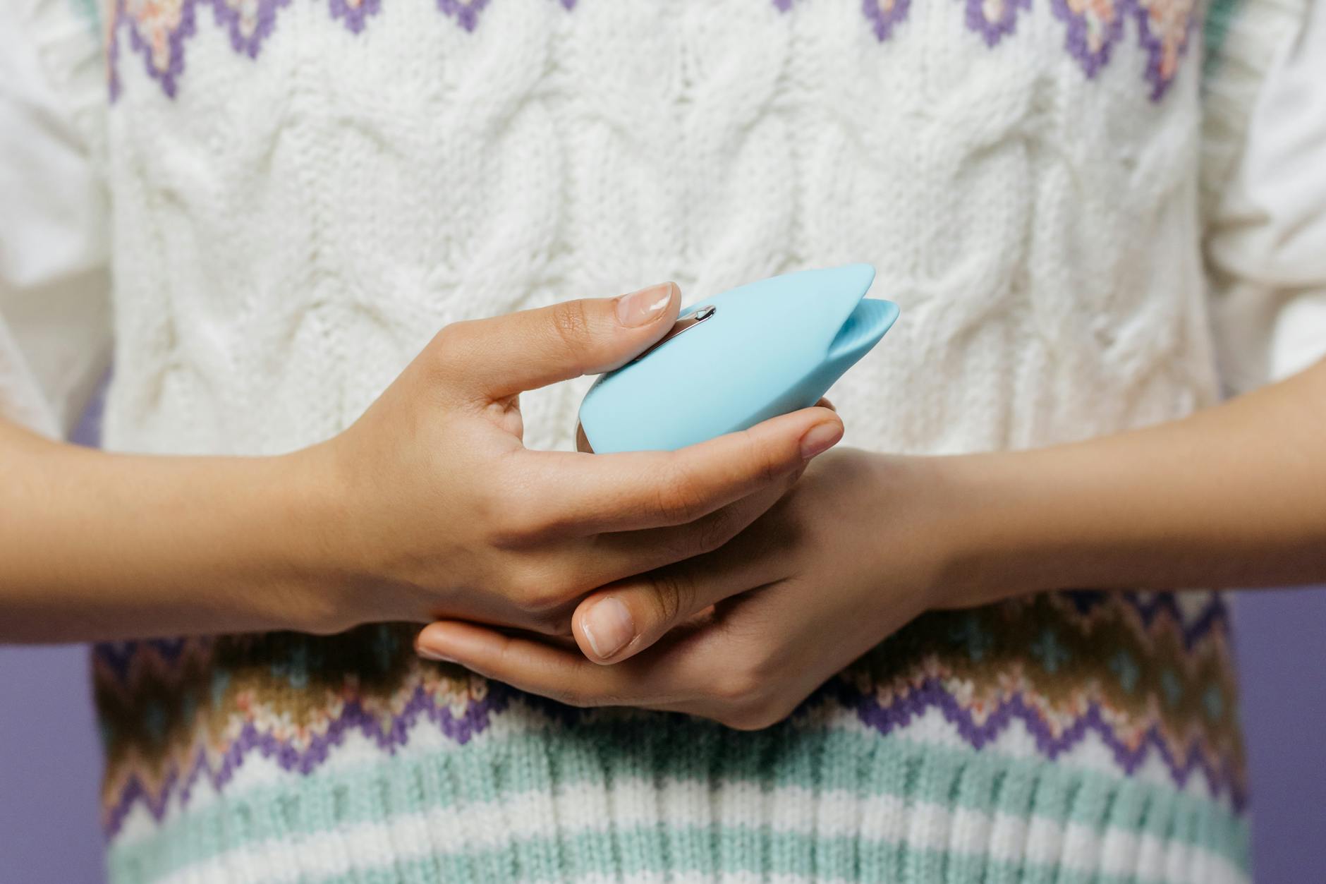 Hand holding a blue silicone vibrator against a solid purple background, symbolizing self-care and sensual recovery